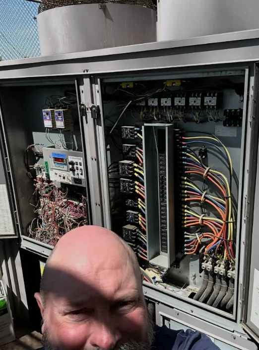 George Blevens in front of an open control cabinet with contactors, terminal strips and a digital controller