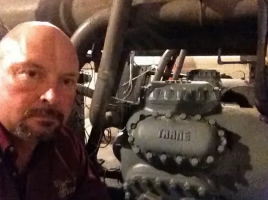 George Blevens beside a reciprocating compressor on a commercial service call