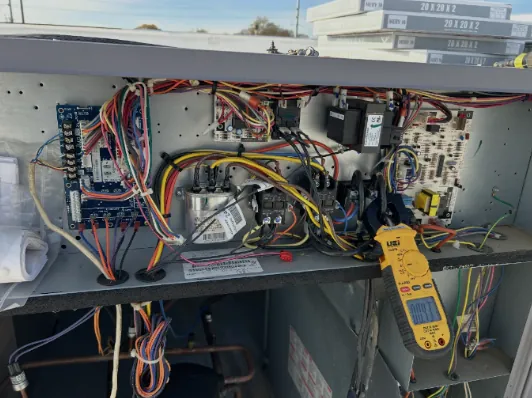 Rooftop unit control compartment with control boards, a run capacitor, contactors and a clamp meter on one lead