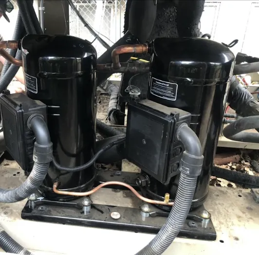 Two black scroll compressors mounted side by side on a common base in a commercial unit