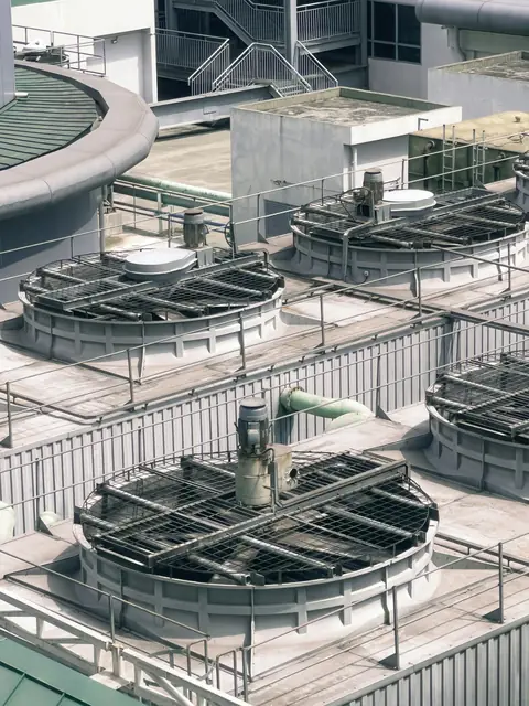 Row of round cooling tower cells with fan motors and guards on a building roof